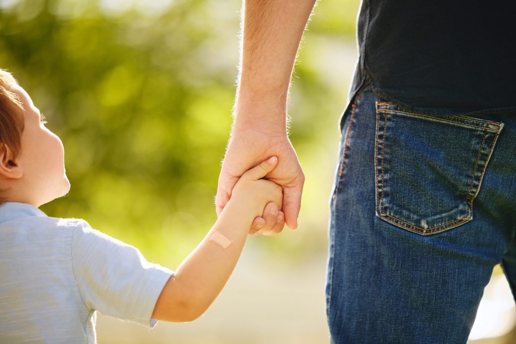 Man, child and holding hands back outdoor park together for bonding, love and support on summer vacation. Father, son and walking with care, trust and morning travel for holiday freedom of memory